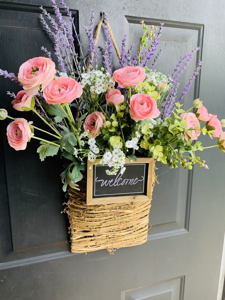 a basket filled with pink flowers sitting on top of a door sill next to a welcome sign