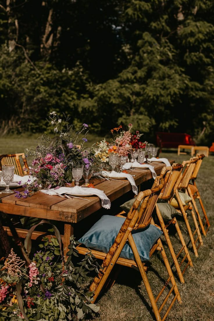 a wooden table topped with lots of flowers next to a forest filled with tall trees