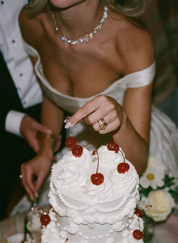 a bride and groom are cutting their wedding cake with cherries on the top tier