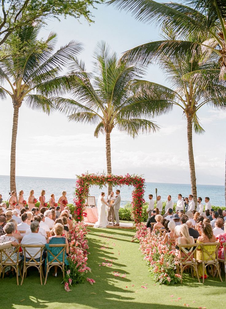 a wedding ceremony at the beach with palm trees and people sitting on chairs in front of them