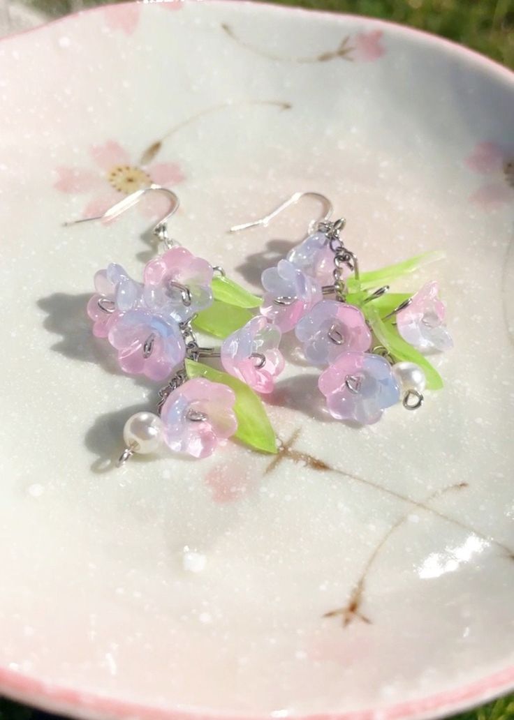 Elevate your style with these exquisite handcrafted glass flower earrings that capture the beauty of nature in a delicate and unique way. Each pair is a wearable piece of art, perfect for expressing your love for botanical beauty and floral elegance. Product Details: Materials: These glass flower earrings are meticulously crafted using high-quality, translucent glass petals that are both lightweight and durable. The intricate details of the petals give them a lifelike appearance. Design: These dangle earrings feature a stunning floral design with vibrant colors that mimic real blossoms. The glass flowers are carefully shaped and assembled, creating a captivating and three-dimensional effect that's sure to catch everyone's eye. Versatile Style: These earrings are a versatile addition to you Whimsical Iridescent Earrings With Ear Wire, Whimsical Resin Jewelry With Ear Wire, Whimsical Earrings With 3d Flowers For Gift, Whimsical 3d Flowers Earrings For Gifts, Whimsical 3d Flowers Earrings As Gift, Hand Painted Jewelry As Spring Gift, Hand Painted Jewelry For Spring Gift, Unique Flower-shaped Resin Earrings, Handmade Whimsical Jewelry For Spring