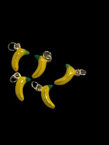 three banana charms are hanging from silver earwires on a black background in the dark