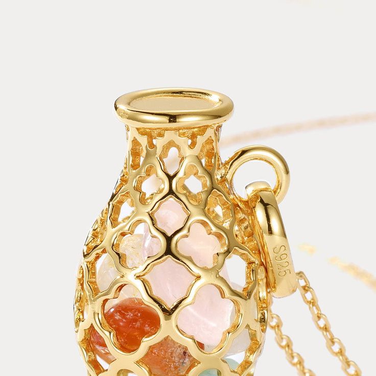 a small vase with hearts on it is sitting on a gold plated chain necklace