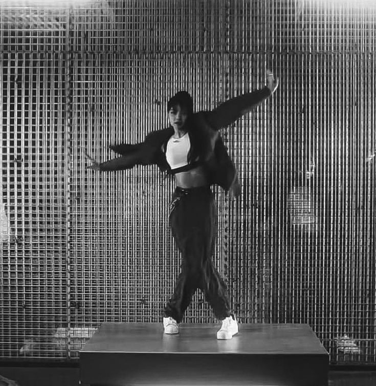 a woman standing on top of a wooden bench in front of a metal screen wall