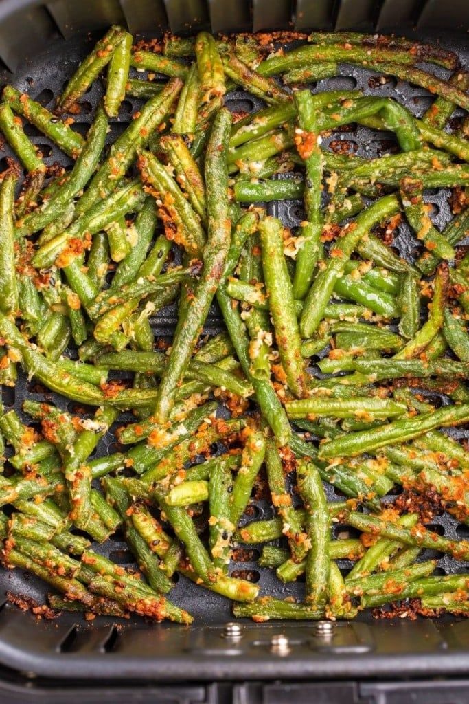 cooked green beans in a black container with seasoning sprinkles on top