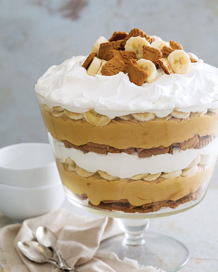 a layered dessert with bananas and whipped cream in a glass dish on a table next to a spoon