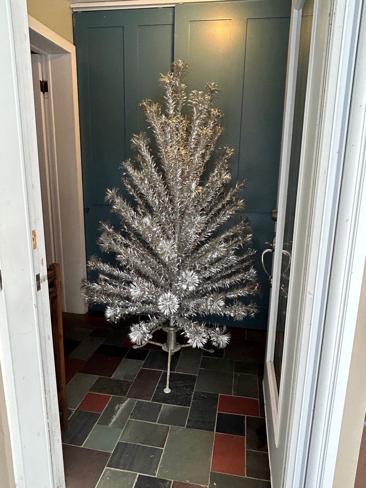 a silver christmas tree sitting on top of a tiled floor next to an open door