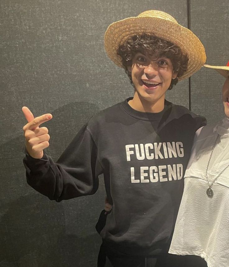 two young people wearing hats and posing for a photo in front of a black wall