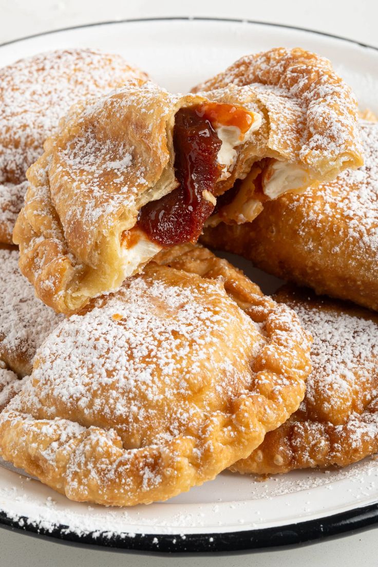 three pastries on a white plate with powdered sugar and jelly filling the edges