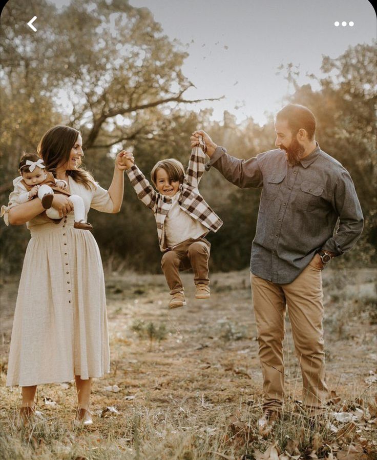 a man and woman holding two children in their hands while they walk through the woods