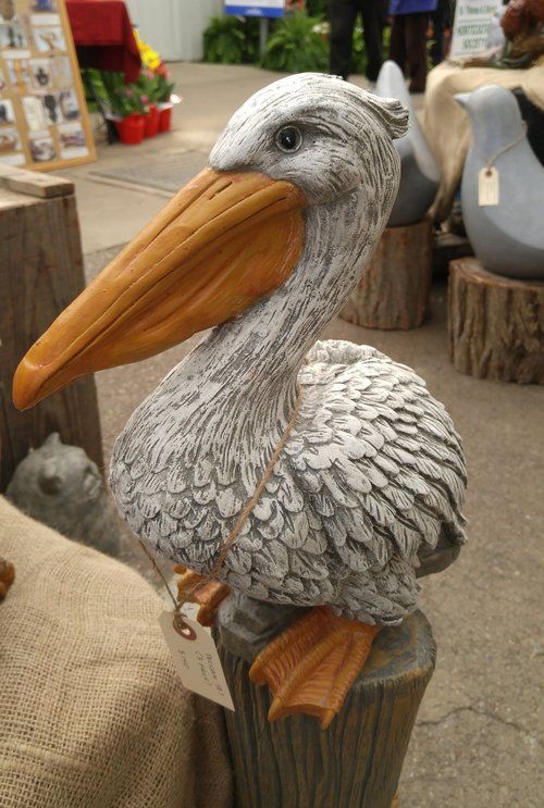 a statue of a pelican sitting on top of a piece of wood with a tag in it's beak