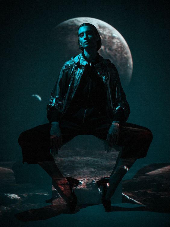 a man sitting on top of a rock in front of a full moon with his legs crossed