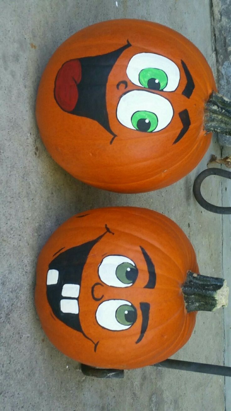 two pumpkins with faces painted on them sitting on the ground next to each other