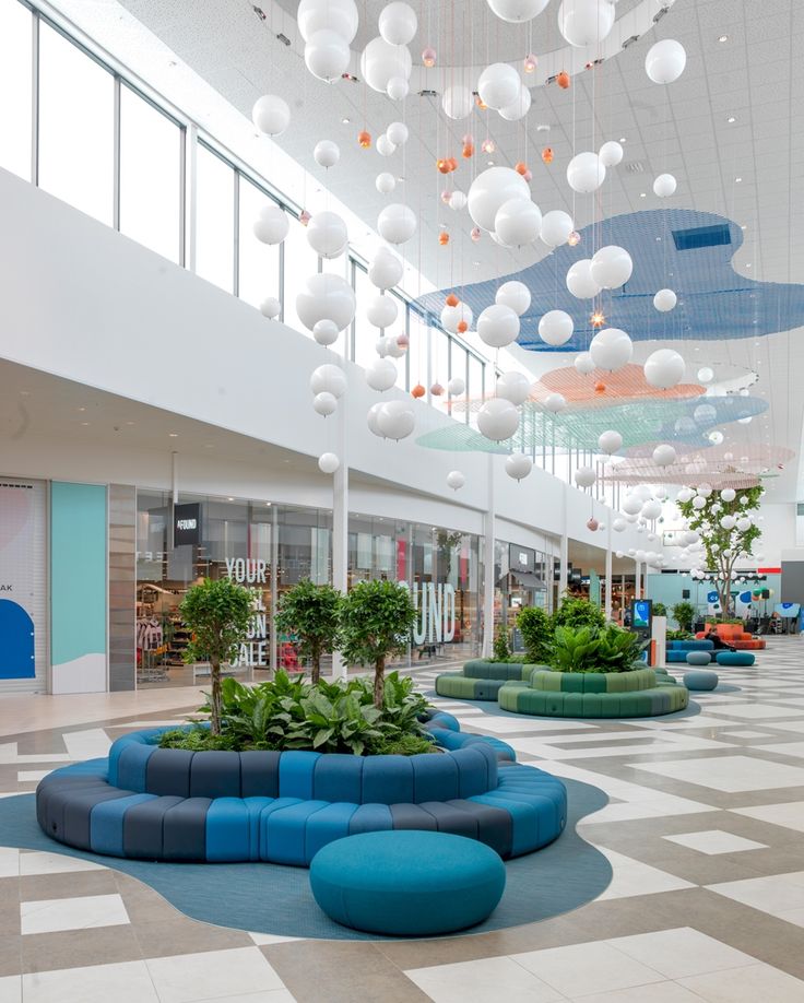 an indoor shopping mall with blue and white seating, plants and lights hanging from the ceiling