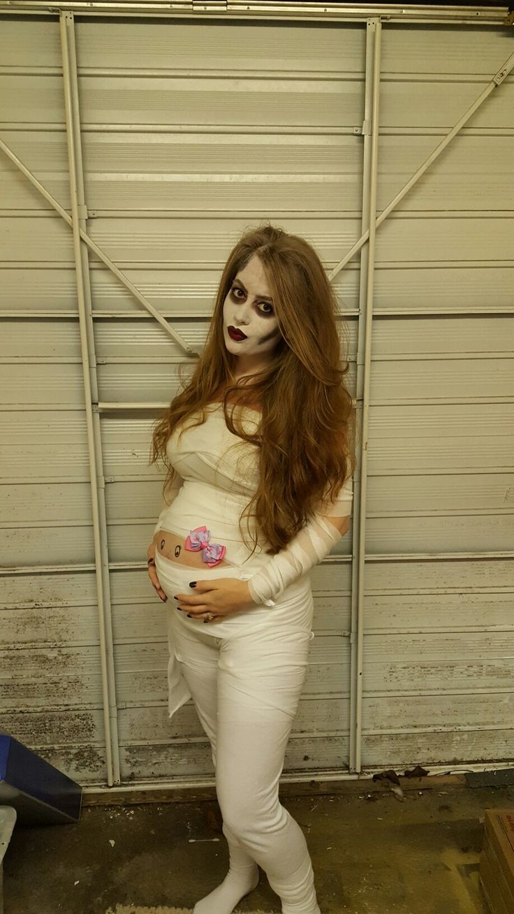 a pregnant woman dressed as a skeleton holding a baby bump in her belly, standing next to a garage door