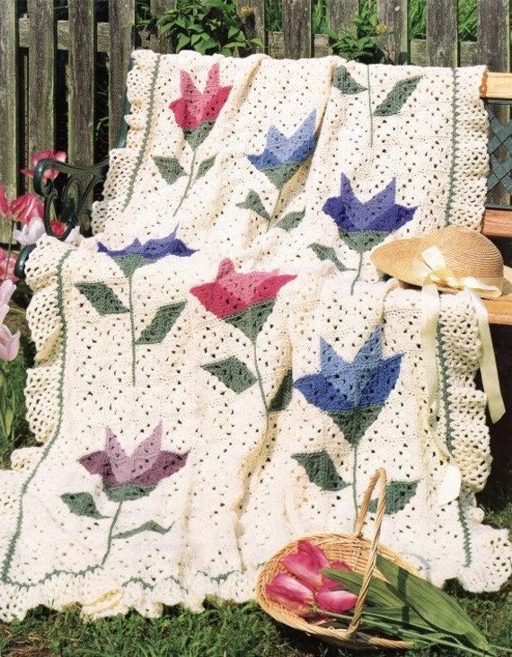 a crocheted blanket sitting on top of a wooden bench next to flowers and a basket