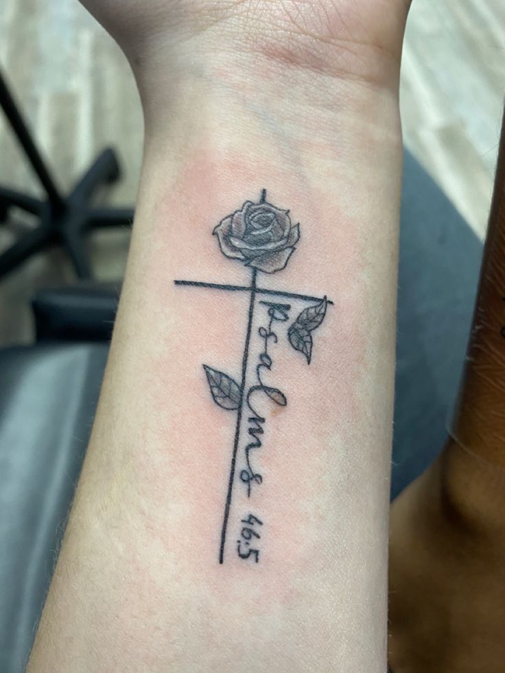 a small cross tattoo on the wrist that says faith and hope with a rose in it