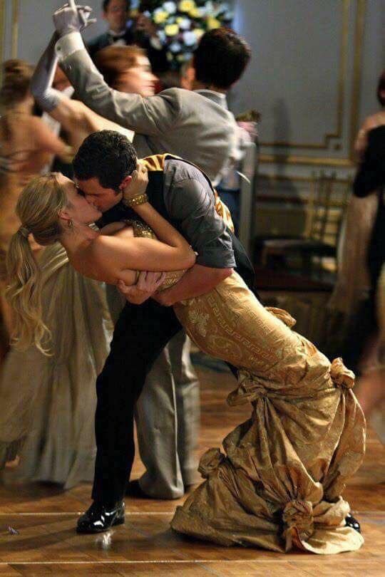 a man and woman kissing on the dance floor with other people in the back ground