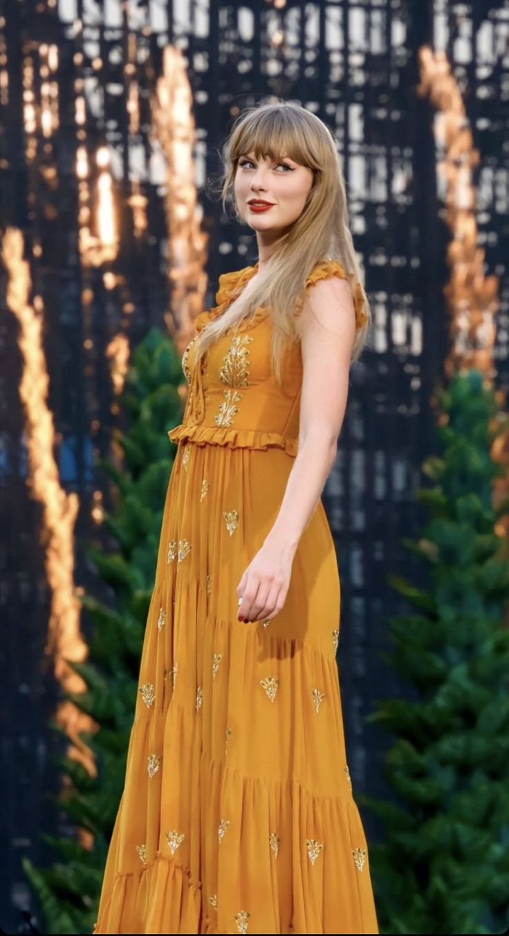 a woman in a yellow dress standing next to a christmas tree with her hand on her hip