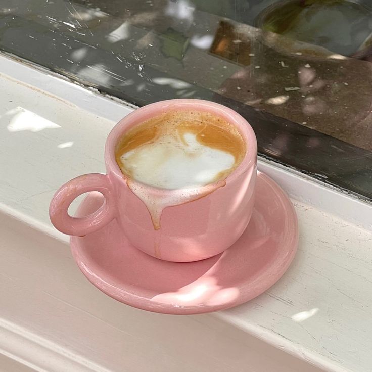 a pink coffee cup sitting on top of a saucer next to a window sill