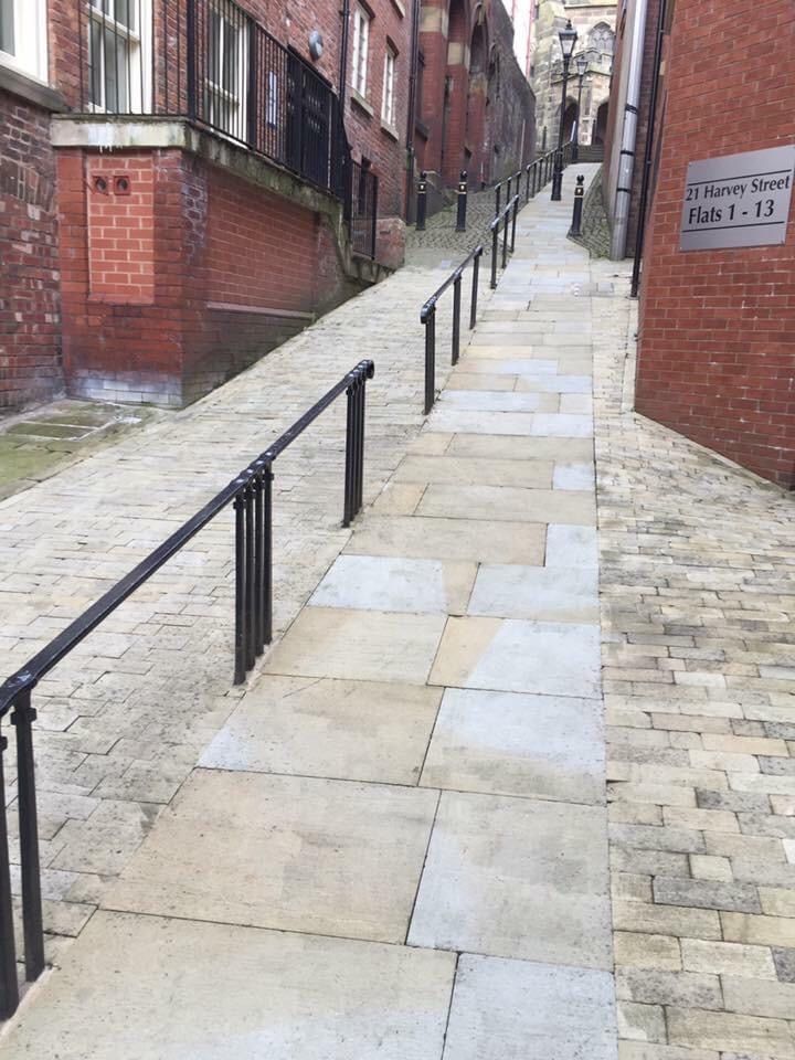 an empty street with brick buildings on both sides and black railings to the right