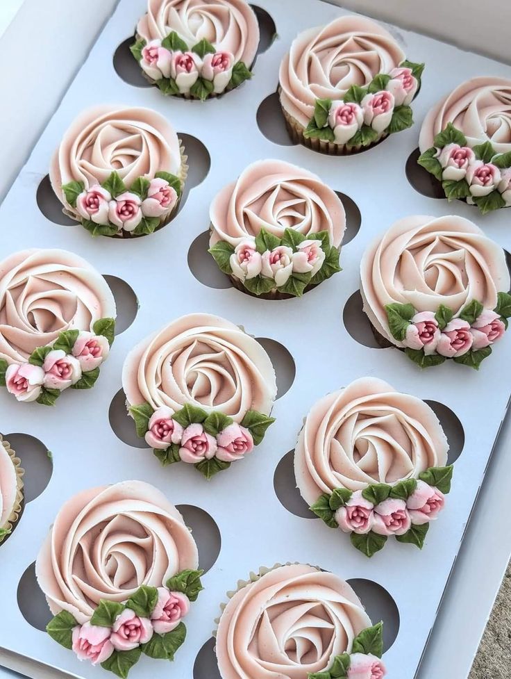 twelve cupcakes with pink frosting and flowers on them in a white box