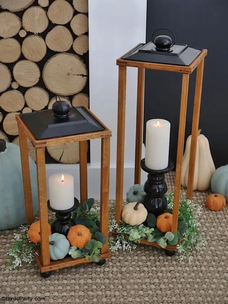 two wooden lanterns sitting next to each other on top of a carpeted floor with pumpkins and greenery