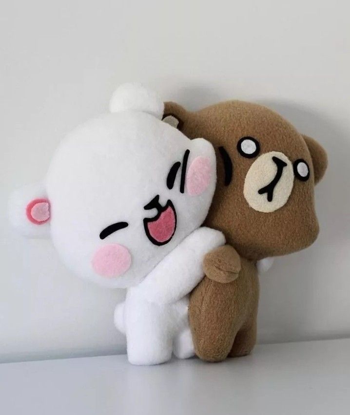 two stuffed bears hugging each other on a white surface, one is brown and the other is pink