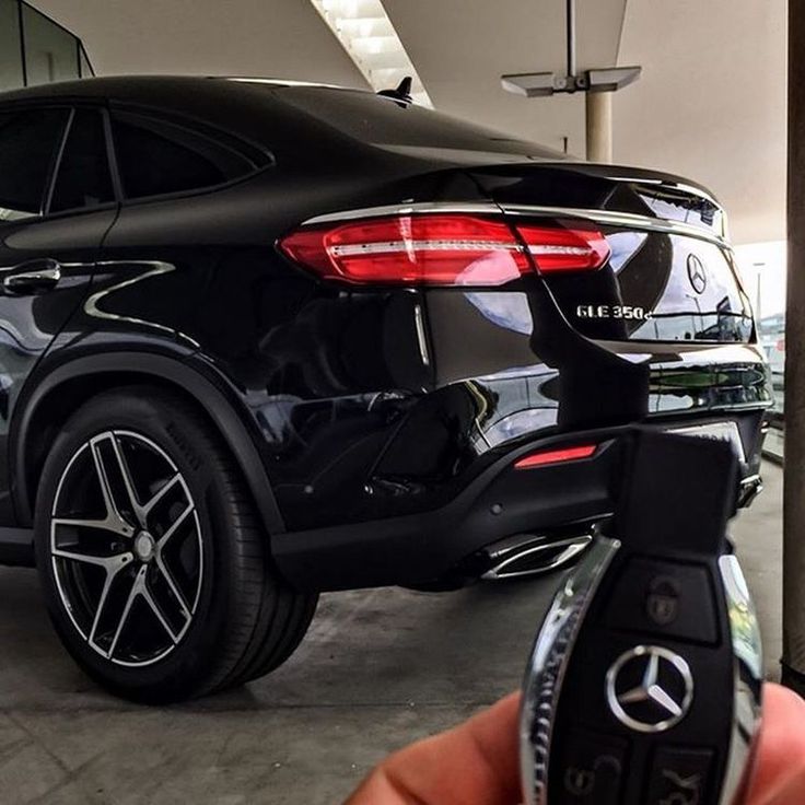 a hand holding a remote control in front of a black mercedes suv parked in a garage