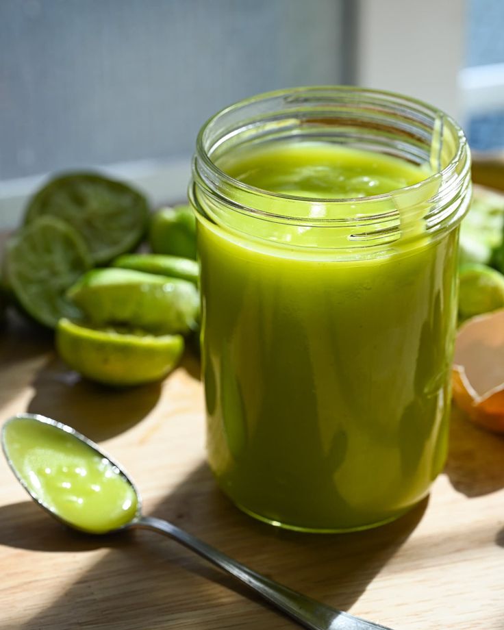 a jar filled with green liquid sitting on top of a wooden table next to sliced oranges