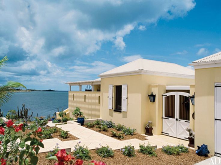 a yellow house next to the ocean with red flowers in front of it and blue sky