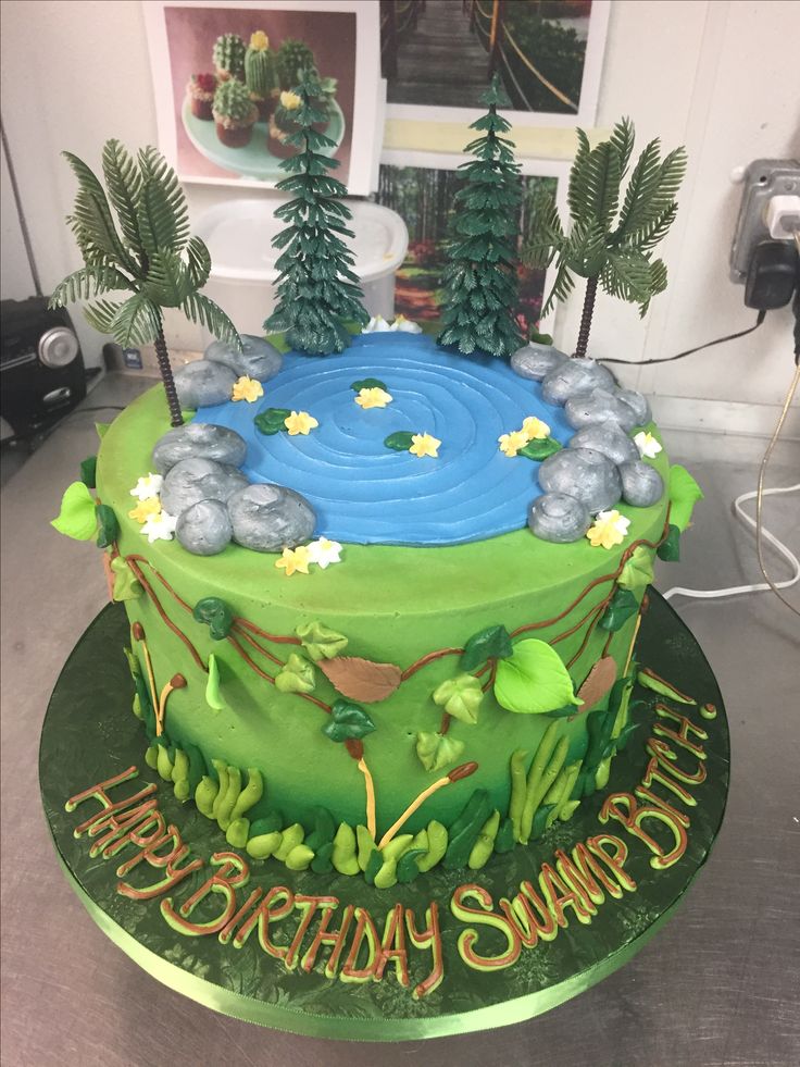 a green birthday cake decorated with trees and water