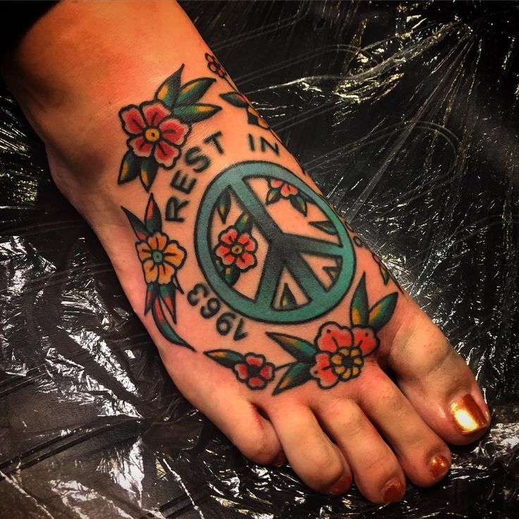 a person's foot with a peace sign tattoo and flowers around the toe area