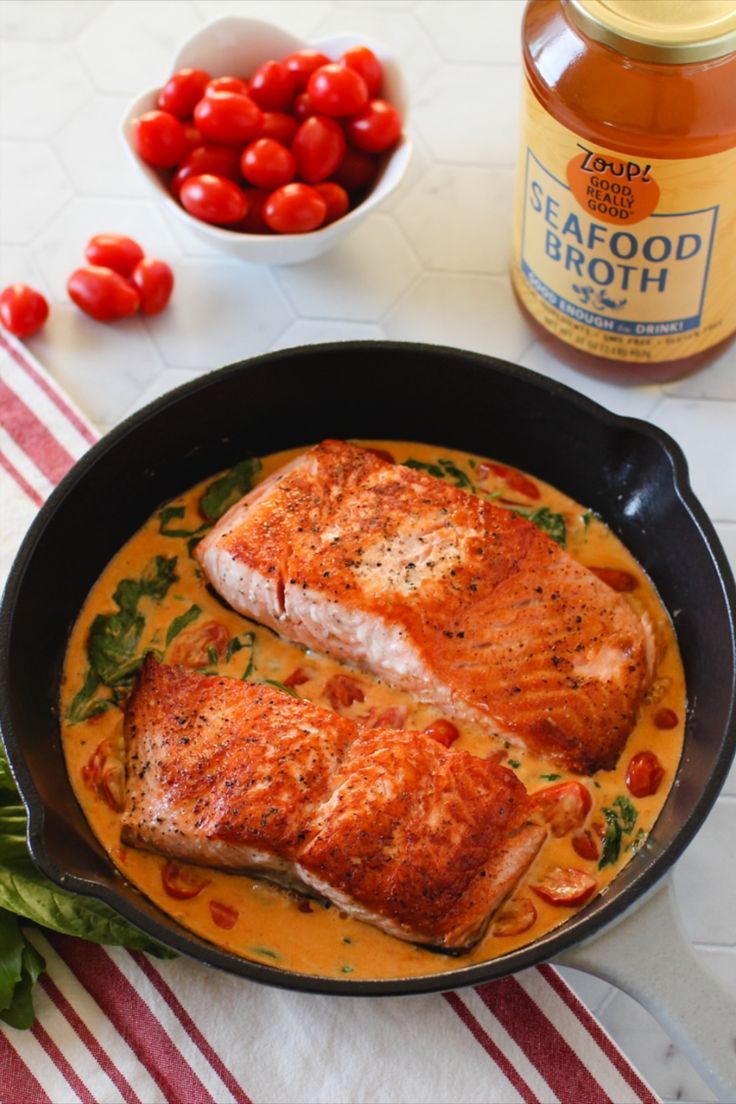 two fish fillets in a skillet with tomatoes and seasoning on the side