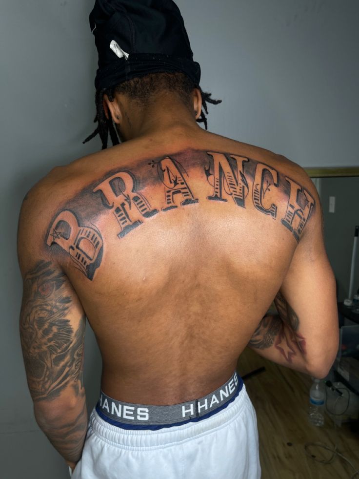 the back of a man with tattoos on his upper and lower half, which reads branch