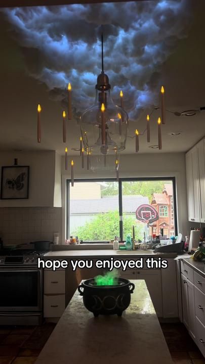 a kitchen with a sky filled with clouds above the counter top and ceiling lights hanging from the ceiling