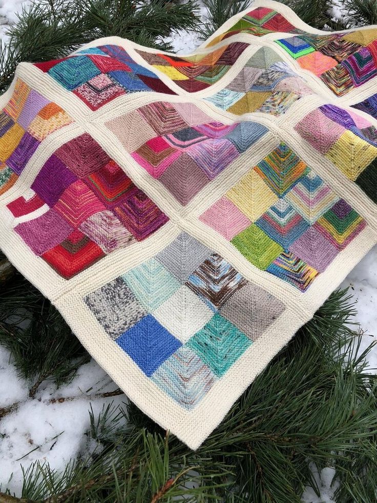 a patchwork quilt is hanging from a tree branch in the snow on a snowy day