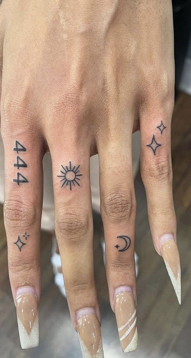 a person's hand with tattoos on it and two fingers that have stars, crescents, and the moon