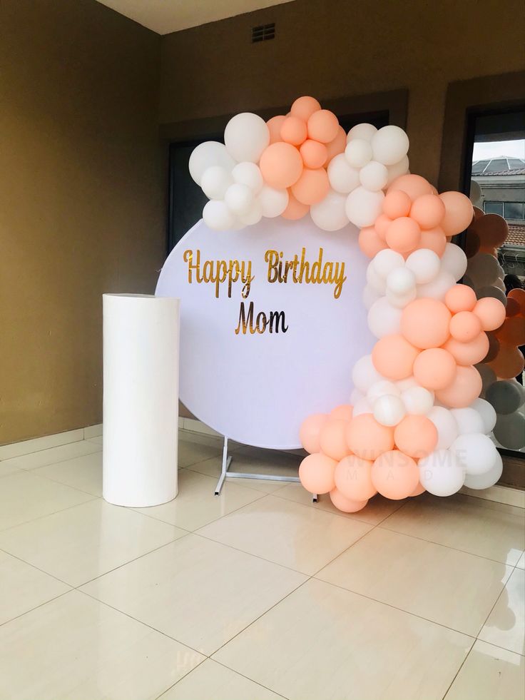 a happy birthday mom balloon arch with white and peach balloons in front of the entrance