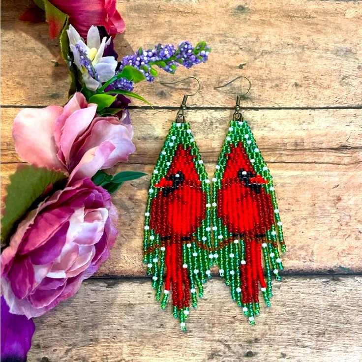 red bird beaded earrings sitting on top of a wooden table next to pink flowers