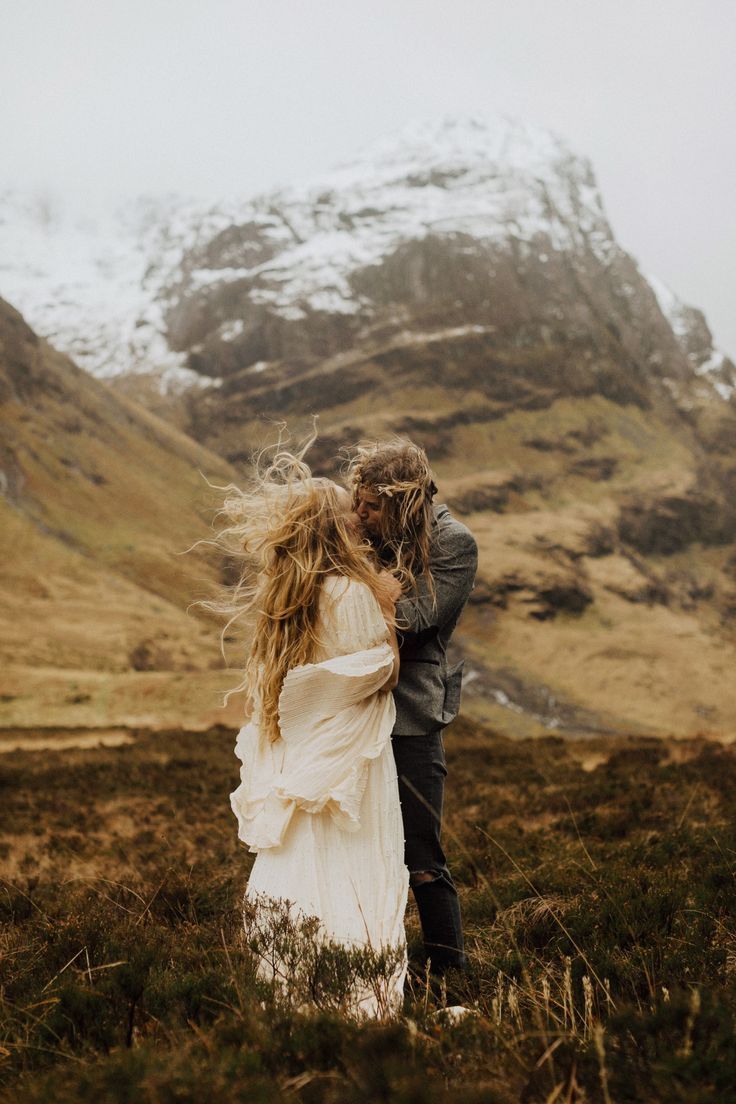 a man and woman standing next to each other in front of a snow covered mountain