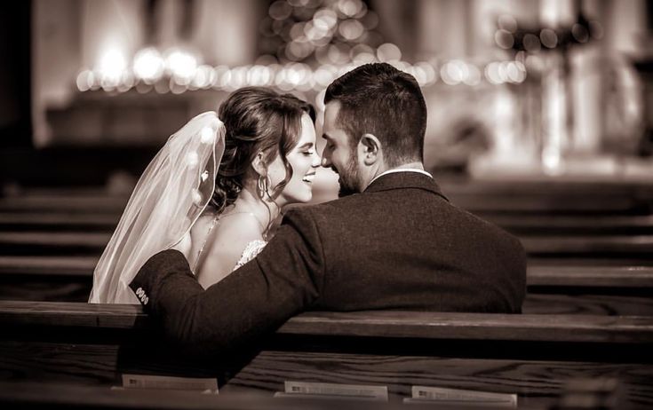 a bride and groom sitting on a bench in front of a building at night with their arms around each other