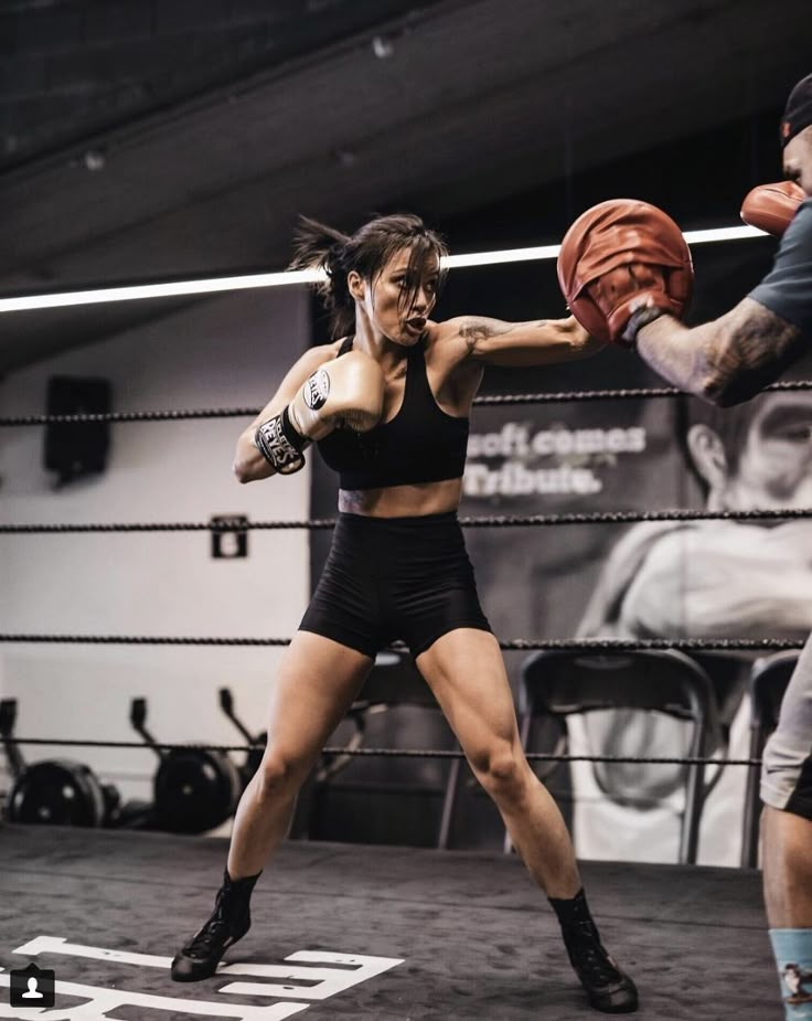 a woman in black shorts and tank top boxing with a man in grey shirt standing next to her