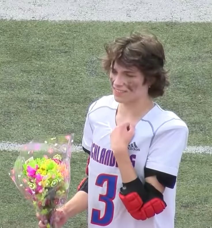 a young man holding flowers on top of a soccer field