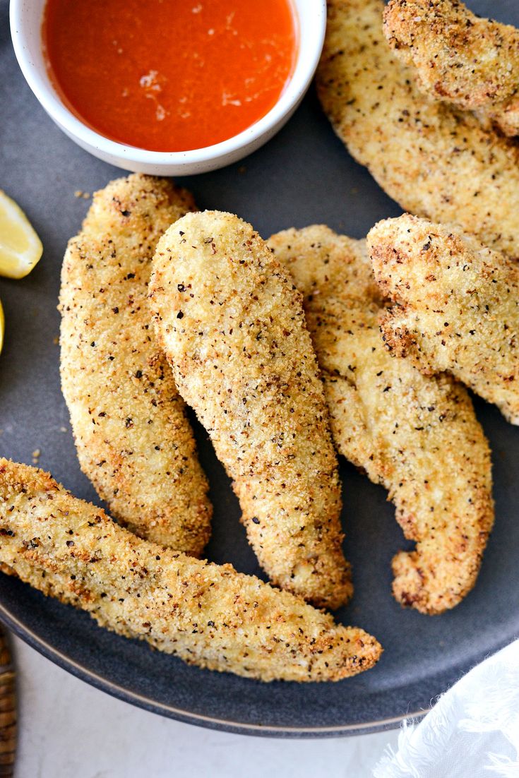 some fried fish sticks are on a plate with sauce and lemon wedges next to it