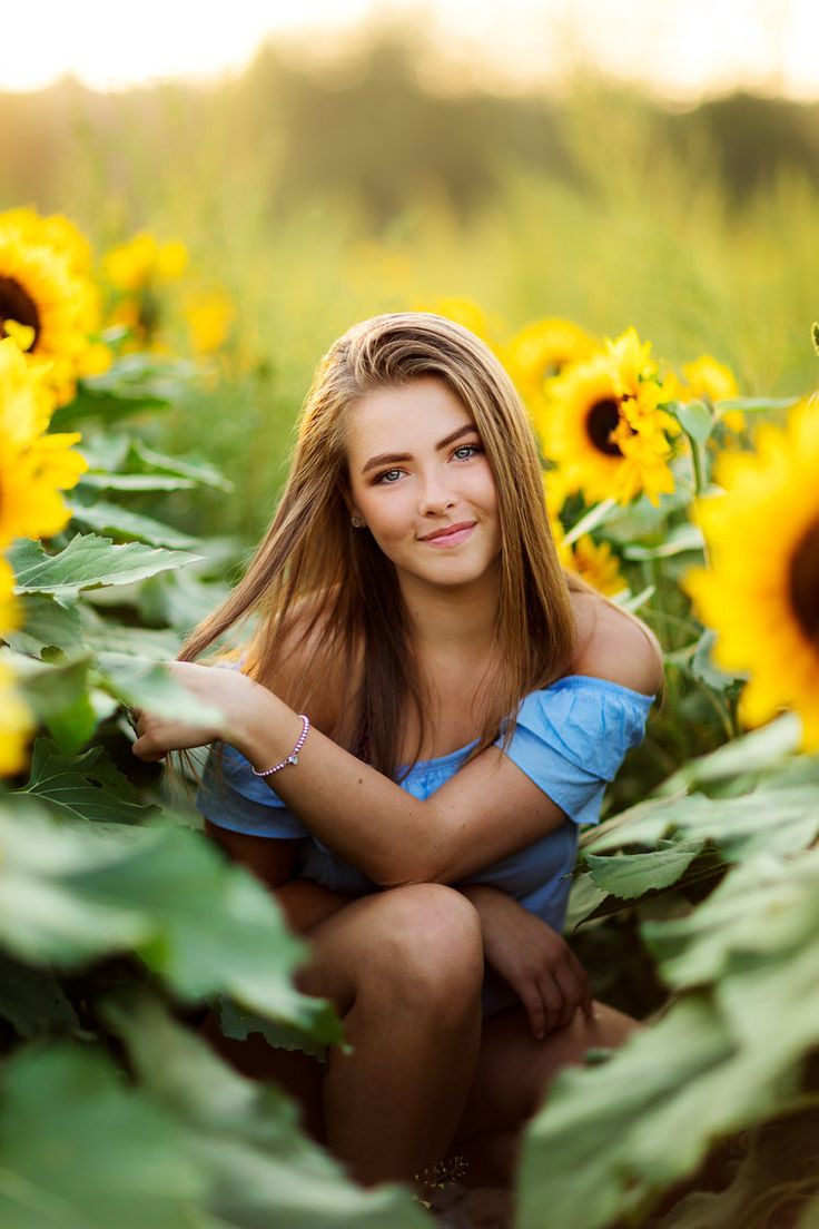 a beautiful young woman sitting in the middle of a sunflower field with her arms crossed