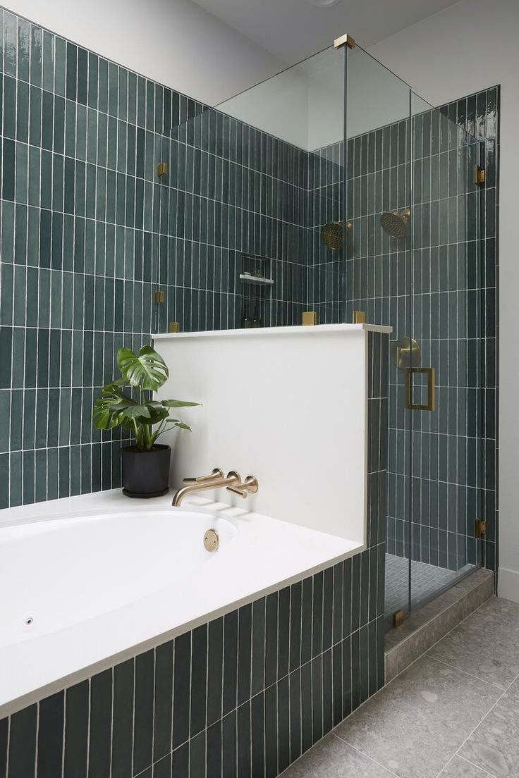 a bath tub sitting next to a green tiled shower stall with a potted plant on it