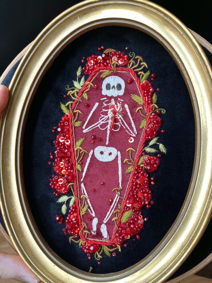 someone is holding up a small embroidery art piece that looks like a skeleton in a frame