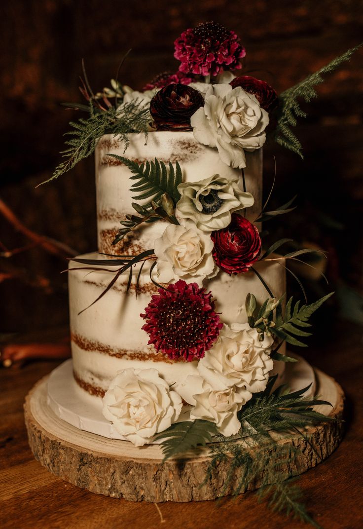 a three tiered cake with flowers and greenery on the top is sitting on a tree stump