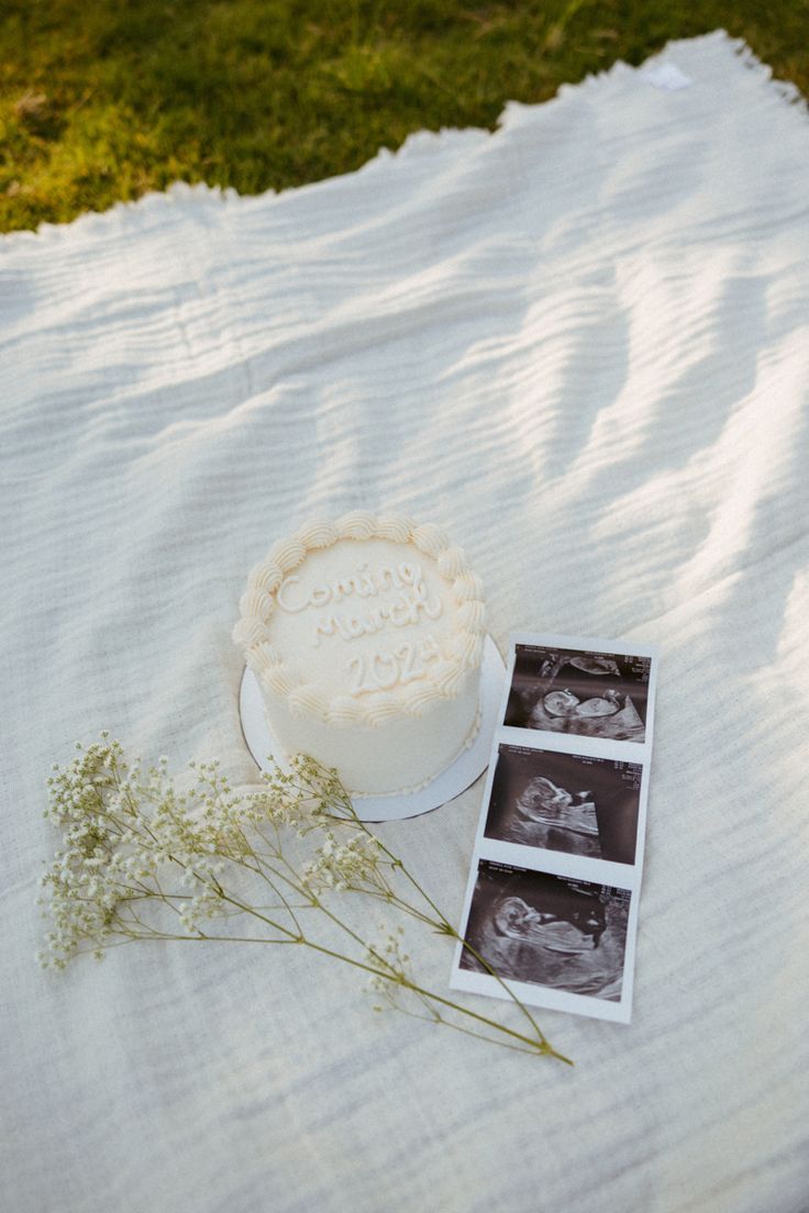 a white cake sitting on top of a blanket next to a flower and two photos